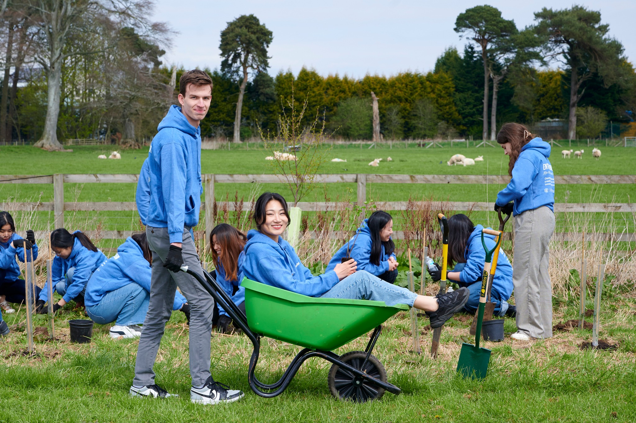 People planting trees with girl being pushed in a wheel barrow